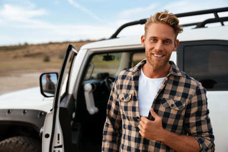 Handsome confident young man posing while standing at his car door at the beach