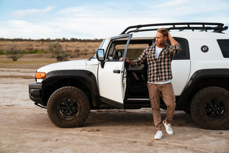 Handsome confident young man posing while standing at his car door at the beachの写真素材