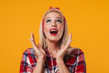 Image of excited blonde pinup girl posing and looking upward isolated over yellow backgroundの写真素材