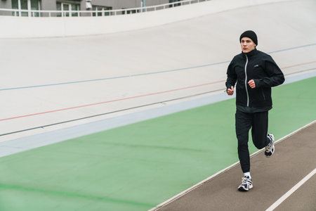 Handsome athletic sportsman running while working out at stadium outdoors