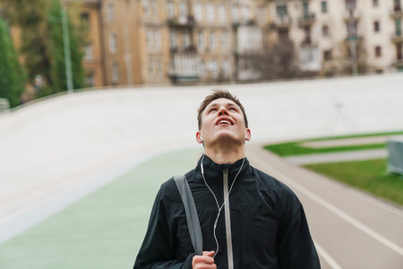 Handsome smiling sportsman listening music with earphones at stadium outdoors
