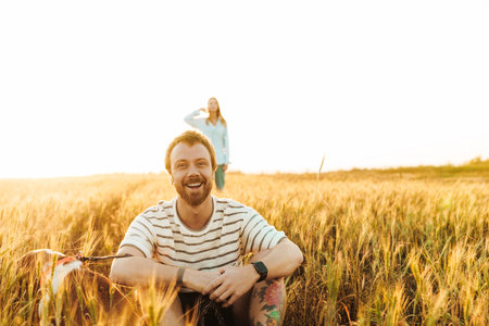Image of handsome happy young man sitting outside at the field while waiting for his girlfriendの写真素材