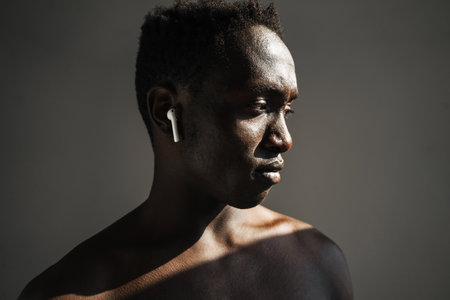 Young african american sportsman using earphones while working out isolated over grey background