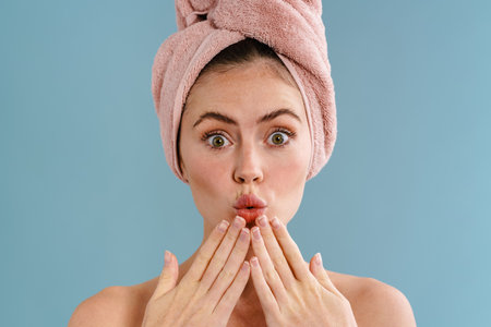 Charming shirtless girl in towel expressing surprise on camera isolated over blue background
