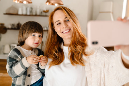 Image of a young happy mother taking a selfie with her son by mobile phoneの写真素材