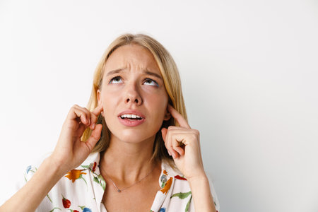 Unhappy beautiful girl plugging her ears while posing at camera isolated over white background
