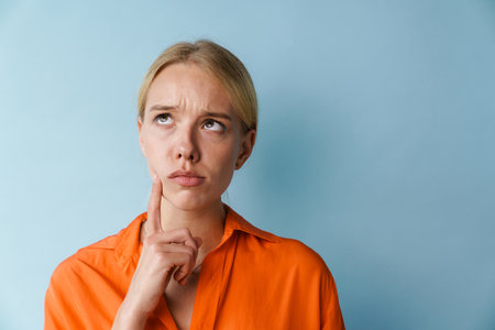 Thinking beautiful blonde girl posing and looking upward isolated over blue background