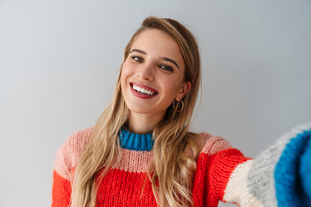 Portrait of a young attractive woman making selfie photo on smartphone isolated on a gray backgroundの写真素材