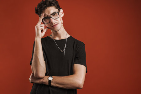 Pensive young hipster man standing isolated over red background