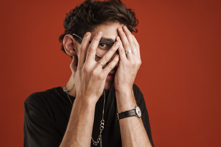 Portrait of a confused man covering his face with palm and looking at camera through fingers...