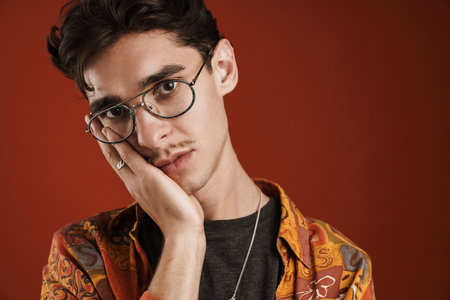 Pensive young hipster teenager in glasses isolated on a red background