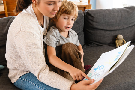 Image of young concentrated pretty woman drawing at home with her son