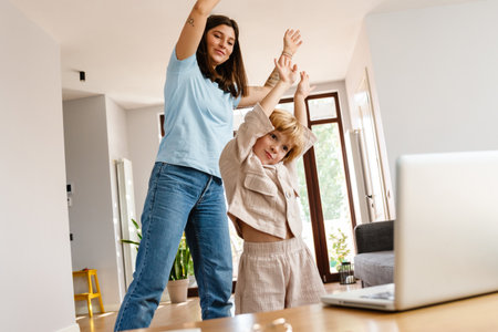 Photo of young positive beautiful woman at home with her son exercising while looking at laptop computerの写真素材