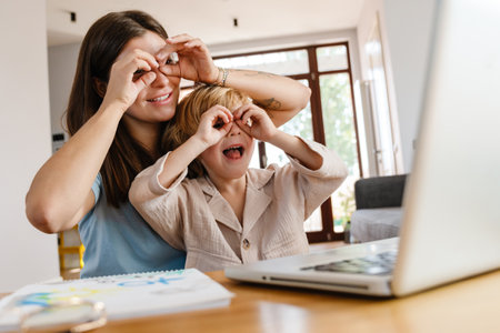 Photo of young funny cute woman at home with her son talking by videocall by laptop computerの写真素材