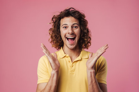 Excited handsome guy pointing expressing surprise on camera isolated over pink backgroundの写真素材