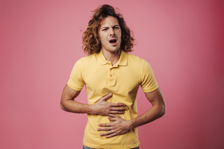 Unhappy handsome guy posing and rubbing his belly isolated over pink backgroundの写真素材