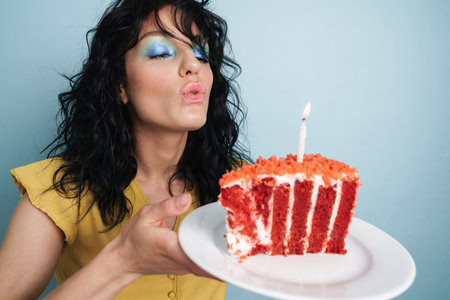 Young happy woman blowing out candle on cake isolated over blue backgroundの写真素材