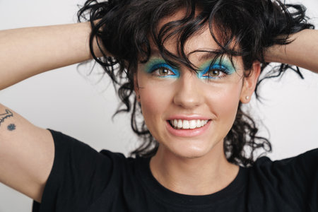 Beauty portrait of an attractive smiling young brunette woman with bright makeup and curly hair isolated over white background, posingの写真素材