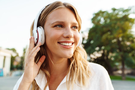 Beautiful happy woman in headphones smiling while walking in green parkの写真素材