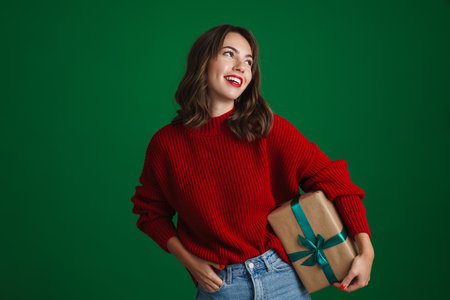 Beautiful joyful nice girl posing with Christmas gift isolated over green backgroundの写真素材