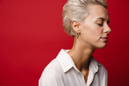 Focused beautiful blonde girl posing posing with eyes closed isolated over red backgroundの写真素材