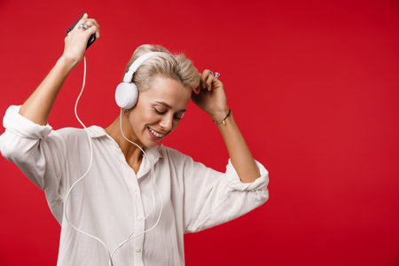 Happy beautiful blonde girl using cellphone and smartphone isolated over red backgroundの写真素材