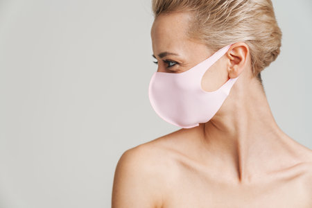 Beautiful shirtless girl in face mask posing on camera isolated over grey backgroundの写真素材