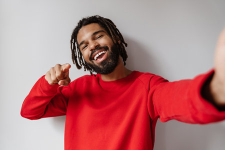 Joyful african american man pointing finger at camera while taking selfie isolated over white backgroundの写真素材