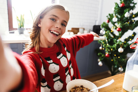 Happy caucasian girl taking selfie photo and showing Christmas tree at home kitchenの写真素材