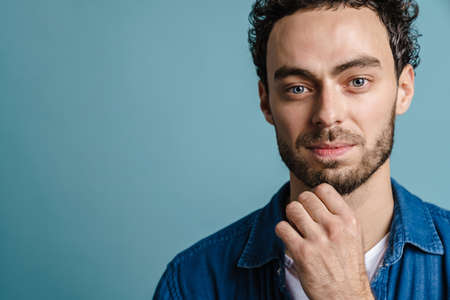 Pleased handsome guy posing and looking at camera isolated over blue background