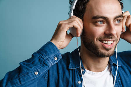 Smiling handsome guy listening music with headphones isolated over blue background