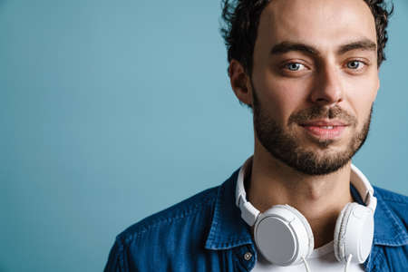 Handsome guy with headphones posing and looking at camera isolated over blue background