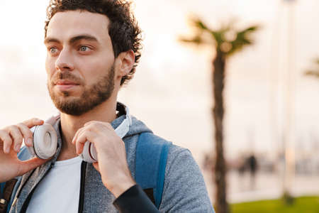 Focused unshaven guy with headphones looking aside while walking on promenadeの写真素材