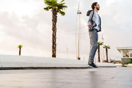 Pleased unshaven guy working out with jump rope on promenadeの写真素材