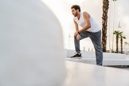 Focused unshaven sportsman resting while working out on promenade