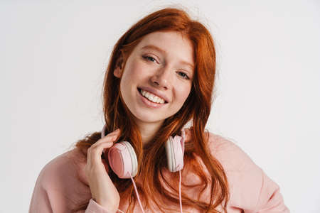 Ginger happy girl with headphones smiling and looking at camera isolated over white background