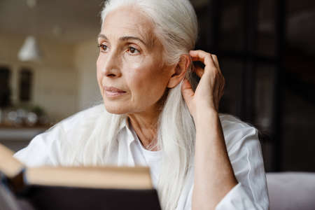 Calm senior woman reading a book while sitting in the living roomの写真素材