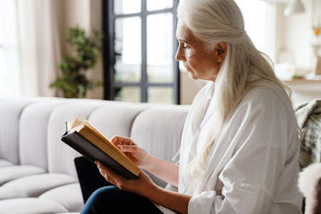 Calm senior woman reading a book while sitting in the living room