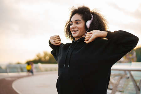 Happy nice sportswoman in headphones doing exercise while working out on city bridgeの写真素材