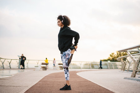 Happy nice sportswoman in headphones doing exercise while working out on city bridgeの写真素材