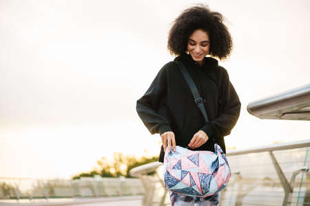 Pleased athletic sportswoman smiling and standing with bag on city bridgeの写真素材