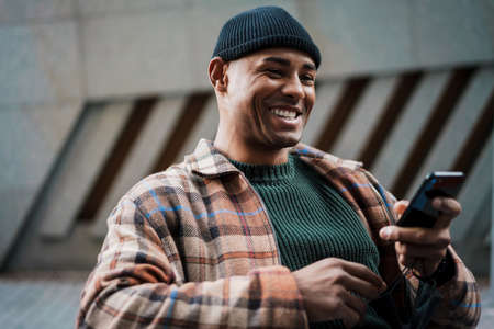 Attractive smiling young african man walking on a street with mobile phoneの写真素材