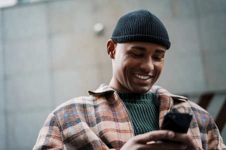 Attractive smiling young african man walking on a street with mobile phoneの写真素材