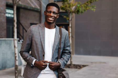 Happy african american man in eyeglasses smiling while walking on streetの写真素材