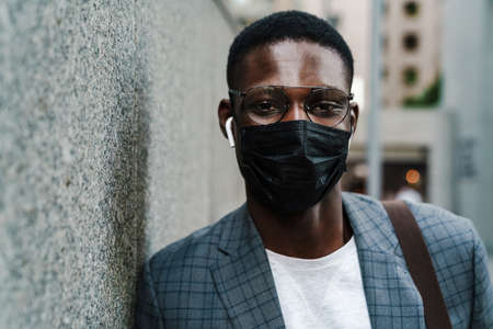 Confident african american man posing in face mask and earphones outdoors