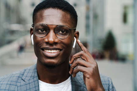 Happy african american man listening music with wireless earphones on city streetの写真素材
