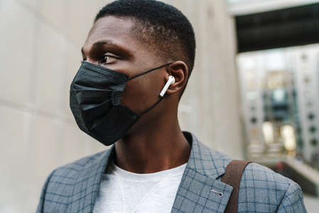 Confident african american man posing in face mask and earphones outdoorsの写真素材