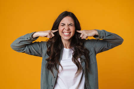 Unhappy beautiful girl grimacing and plugging her ears isolated over yellow backgroundの写真素材