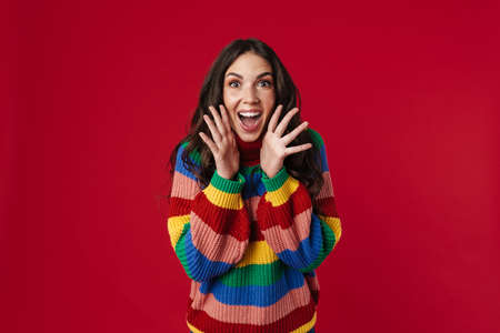 Excited beautiful brunette girl expressing surprise at camera isolated over red background