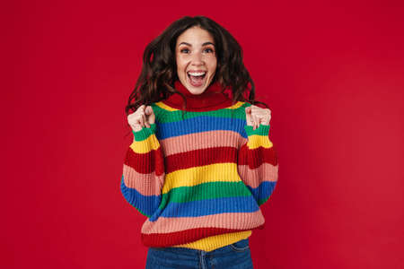 Excited beautiful brunette girl posing with clinched fists isolated over red backgroundの写真素材